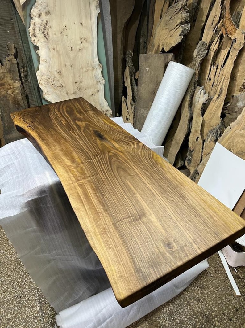 May include: A large, natural wood slab with a live edge. The wood is a rich brown color with a natural grain pattern. The slab is smooth and polished, and it would be perfect for a table top or countertop.