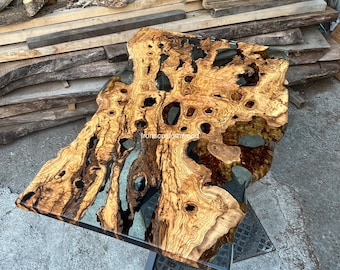 May include: A large, natural wood table top with a clear epoxy resin finish. The wood has a unique grain pattern and several knots. The table top is supported by a black metal base.