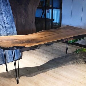 May include: A live edge wooden table with a dark brown finish. The table is supported by black hairpin legs. The table's dimensions are approximately 72 inches long and 30 inches wide.