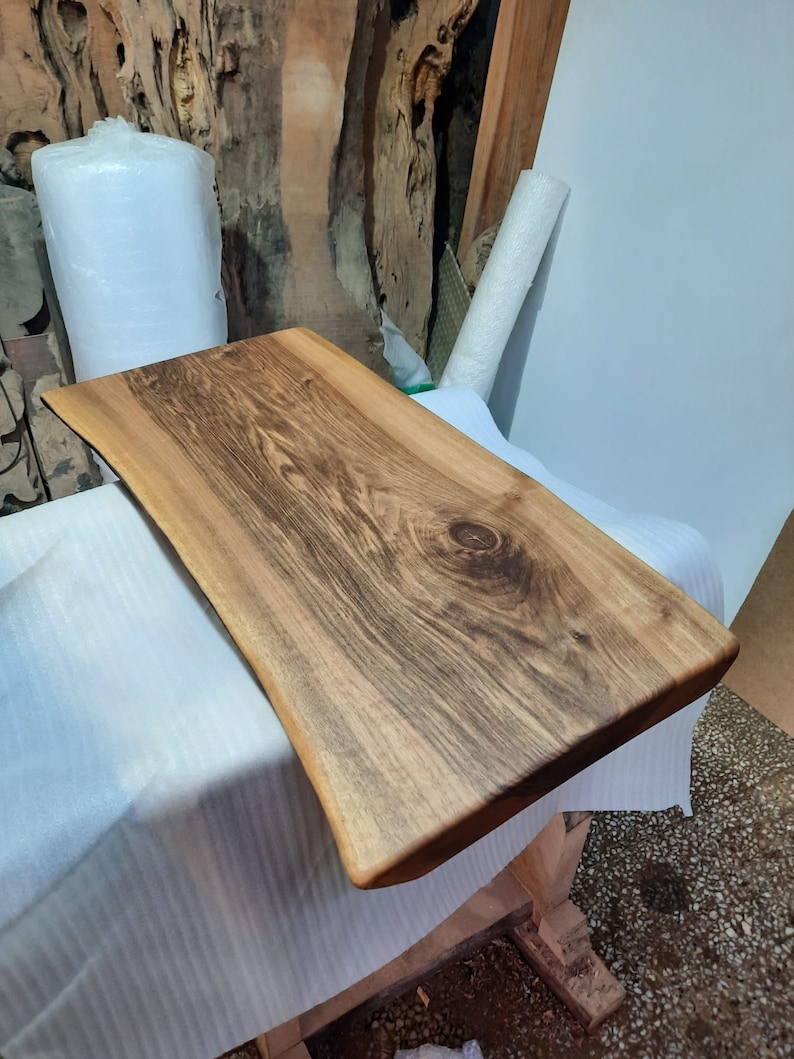May include: A rectangular wooden serving board with a natural edge. The board is made of light brown wood with dark brown grain patterns. The board is approximately 24 inches long and 12 inches wide. The wood has a smooth, polished finish.