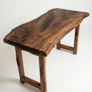 May include: A handcrafted wooden table with a live edge design. The table is made of dark brown wood and features a rectangular top supported by four sturdy legs. The table measures approximately 152 cm long and 51 cm wide.