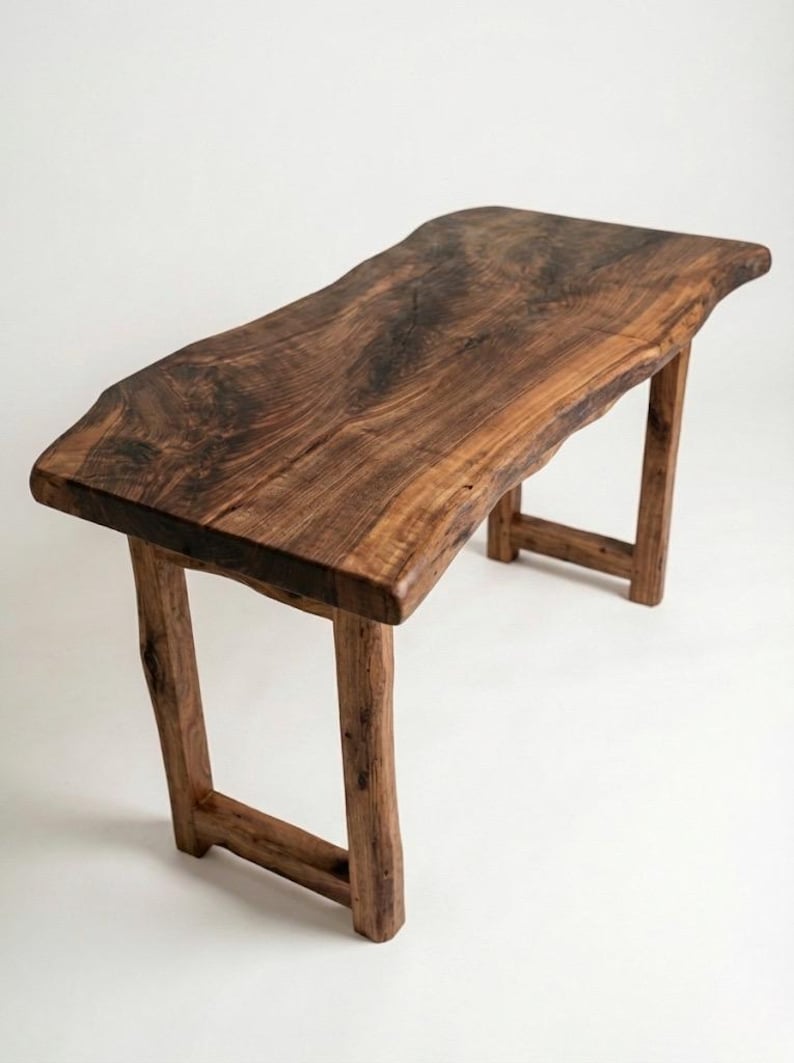 May include: A handcrafted wooden table with a live edge design. The table is made of dark brown wood and features a rectangular top supported by four sturdy legs. The table measures approximately 152 cm long and 51 cm wide.