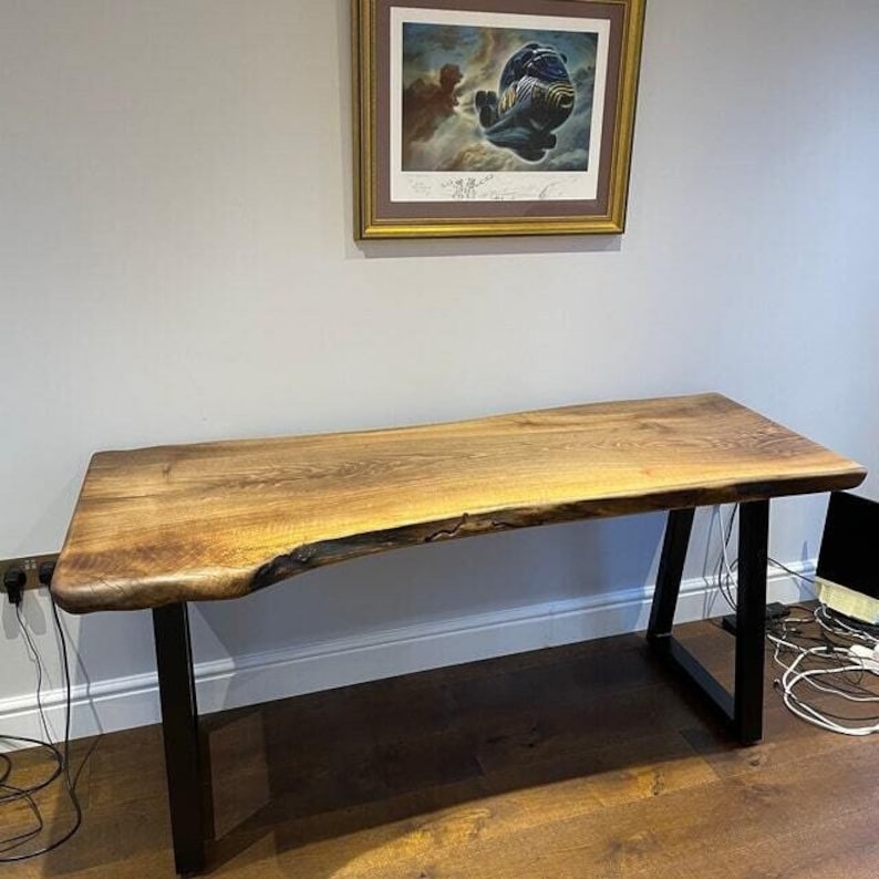 May include: A rustic wooden desk with a live edge top and black metal A-frame legs. The desk is made of natural wood with a warm brown color and a unique grain pattern.