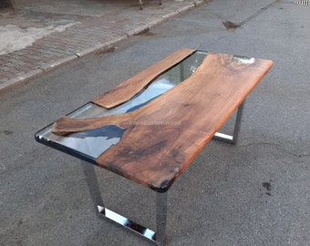 Op de afbeelding: Een rechthoekige houten tafel met een live edge design en een heldere epoxy rivier. De tafel heeft een donkerbruine houtnerf en staat op gepolijste chromen poten. De tafel is ongeveer 183 cm lang.