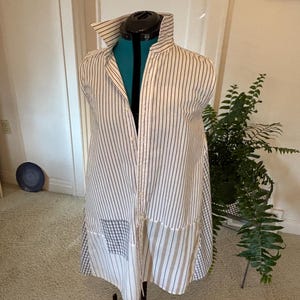 May include: A sleeveless button-down shirt featuring a white base with thin vertical black stripes. The lower portion of the shirt incorporates contrasting panels of light gray and white gingham check fabric and wider beige and white vertical stripes.