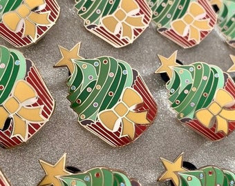 May include: A collection of Christmas tree enamel pins. Each pin features a green tree with white dots, a yellow bow, and a gold star on top. The base is red with white stripes, and the pins have gold-colored metal borders.