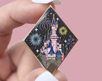 Könnte beinhalten: Ein rautenförmiger Emaille-Pin mit einem rosa und blauen Schloss mit Feuerwerk vor einem schwarzen Nachthimmel. Der Pin hat einen goldenen Rand und ist ein Sammlerstück.