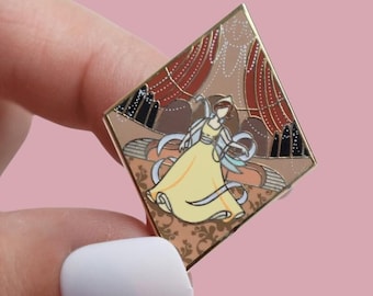 Könnte beinhalten: Goldfarbene Emaille-Anstecknadel in Diamantform. Die Nadel zeigt eine Frau in einem gelben Kleid mit Bändern, vor dem Hintergrund roter Vorhänge und eines gemusterten Bodens. Die Nadel wird vor einem rosa Hintergrund gehalten.