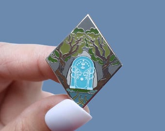 May include: A diamond-shaped enamel pin featuring a blue arched doorway framed by green trees. The pin has a silver border and a light blue background. The design evokes a fantasy theme.