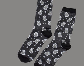 Puede incluir: Un par de calcetines grises oscuros con un patrón repetido de fantasmas y estrellas blancas. Los calcetines tienen talones y dedos negros, y el texto "92ime" está impreso en la parte inferior de cada calcetín.