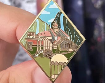 Könnte beinhalten: Goldfarbene, rautenförmige Emaille-Anstecknadel mit einer detaillierten Illustration eines Gebäudes mit rotem Dach, Wasserfällen und blauem Himmel mit Wolken. Die Anstecknadel hat einen goldenen Rand und einen dekorativen Pavillon.