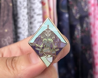 May include: A diamond-shaped enamel pin featuring a stylized figure with a mountain backdrop. The pin has a gold border and a color palette of blues, purples, and greens. The figure is seated, with a serene expression.