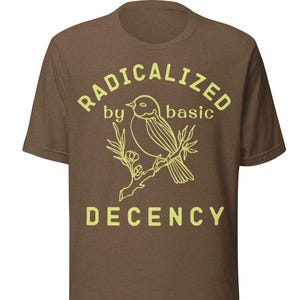 Könnte beinhalten: Braunes T-Shirt mit dem Text "RADICALIZED by basic DECENCY" in Hellgelb. Eine hellgelbe Umrisszeichnung eines Vogels auf einem Ast ist unter dem Text zentriert.
