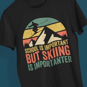 Pode incluir: Camiseta preta com um gráfico retrô de um esquiador nas montanhas. O texto diz "A escola é importante, mas esquiar é mais importante."