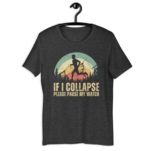 May include: A dark heather grey t-shirt with a vintage-style graphic of a runner in front of a mountain range. The text "IF I COLLAPSE PLEASE PAUSE MY WATCH" is printed below the graphic.