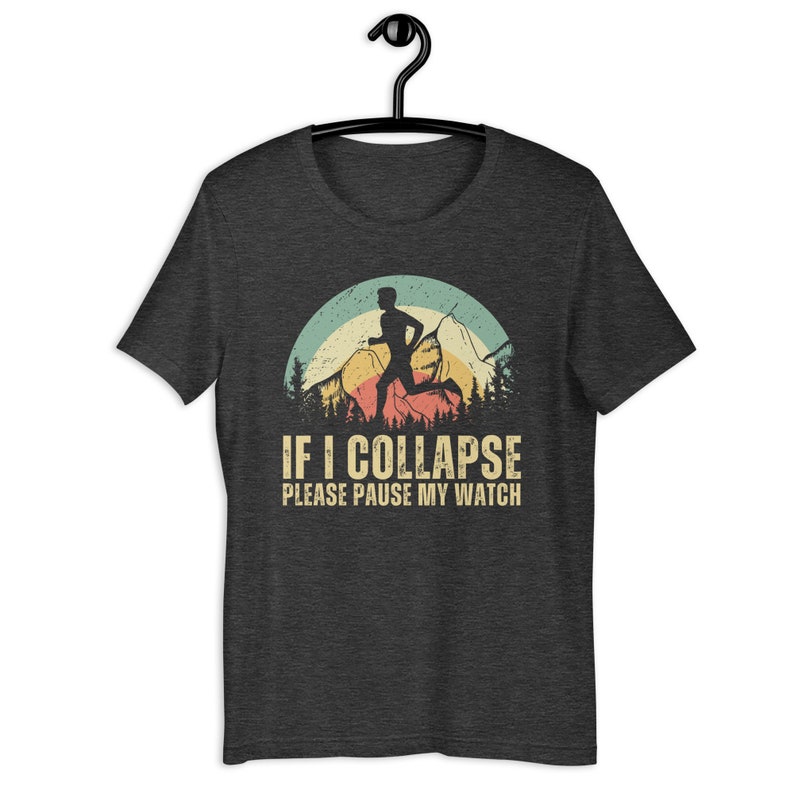 May include: A dark heather grey t-shirt with a vintage-style graphic of a runner in front of a mountain range. The text "IF I COLLAPSE PLEASE PAUSE MY WATCH" is printed below the graphic.