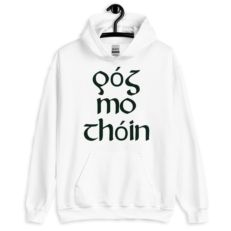 Puede incluir: Sudadera con capucha blanca con bolsillo delantero y cord&oacute;n. La sudadera presenta texto verde oscuro en una fuente estilizada. El texto dice "G&oacute;s mo ch&oacute;in". La sudadera est&aacute; colgada de una percha negra.