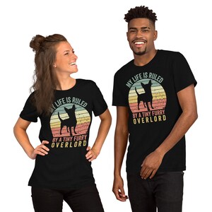 Op de afbeelding: Twee mensen dragen zwarte T-shirts met een vintage-stijl afbeelding van een chihuahua en de tekst "Mijn leven wordt geregeerd door een kleine harige overlord".