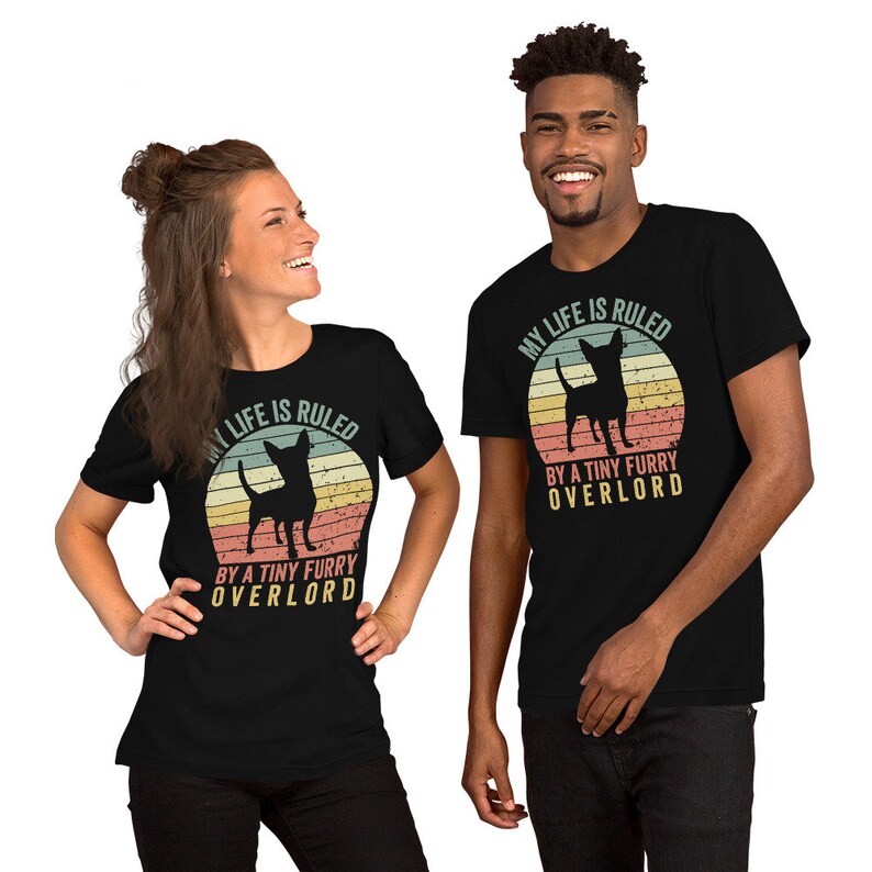 Op de afbeelding: Twee mensen dragen zwarte T-shirts met een vintage-stijl afbeelding van een chihuahua en de tekst "Mijn leven wordt geregeerd door een kleine harige overlord".