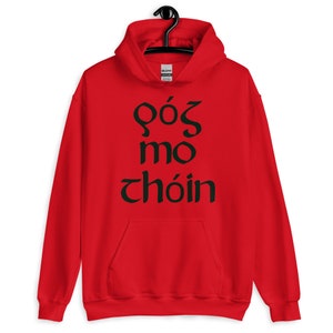 Puede incluir: Sudadera roja con capucha, bolsillo delantero y cord&oacute;n ajustable. La sudadera presenta texto verde oscuro en una fuente estilizada, posiblemente celta. La prenda est&aacute; colgada de una percha negra.
