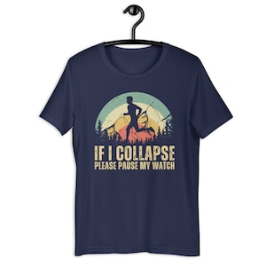 May include: Navy blue t-shirt with a vintage-style graphic of a runner in front of a mountain range with a sunset behind them. The text "IF I COLLAPSE PLEASE PAUSE MY WATCH" is printed below the graphic.