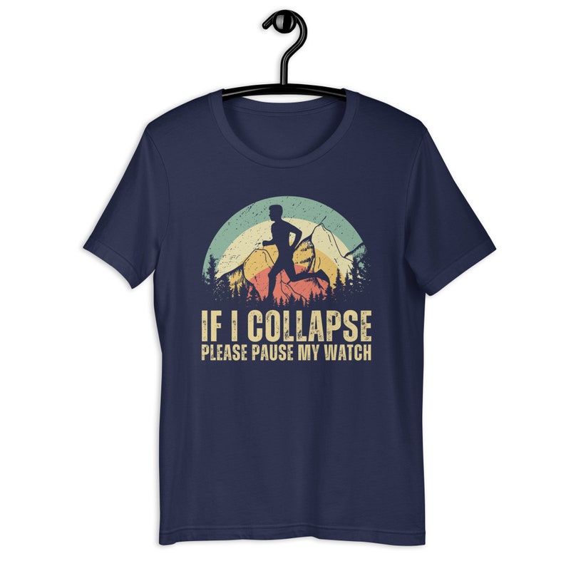 May include: Navy blue t-shirt with a vintage-style graphic of a runner in front of a mountain range with a sunset behind them. The text "IF I COLLAPSE PLEASE PAUSE MY WATCH" is printed below the graphic.