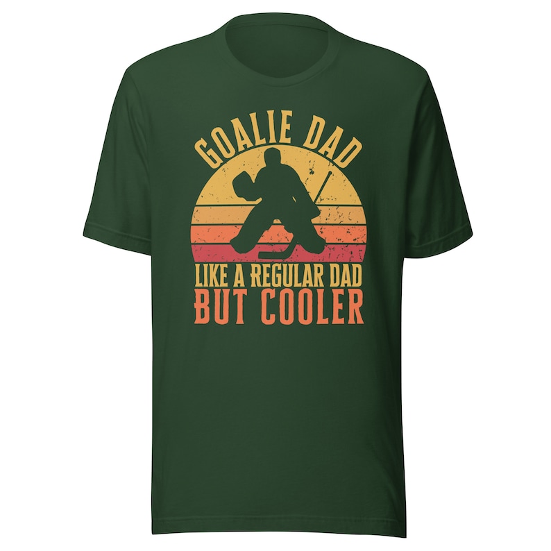 May include: Green t-shirt with a retro-style graphic of a hockey goalie in front of a sunset. The text reads "Goalie Dad Like a Regular Dad But Cooler".