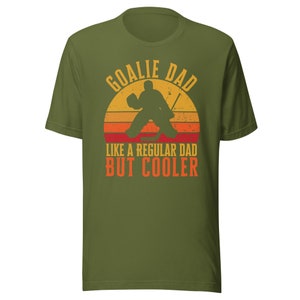 May include: Green t-shirt with a retro-style graphic of a hockey goalie with the text "Goalie Dad Like a Regular Dad But Cooler".