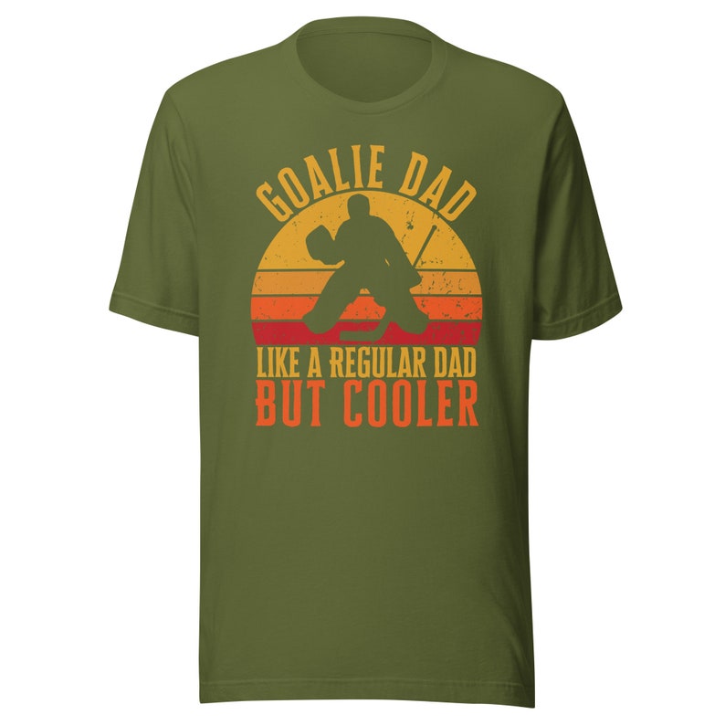 May include: Green t-shirt with a retro-style graphic of a hockey goalie with the text "Goalie Dad Like a Regular Dad But Cooler".