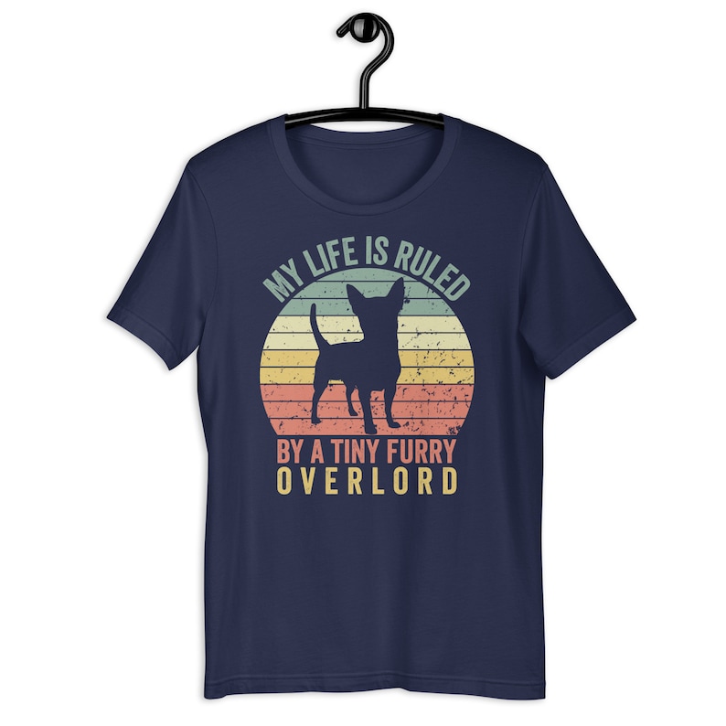 Op de afbeelding: Donkerblauw T-shirt met een vintage-stijl grafische afbeelding van een chihuahua-silhouet voor een zonsondergang. De tekst luidt "Mijn leven wordt geregeerd door een kleine harige overlord."