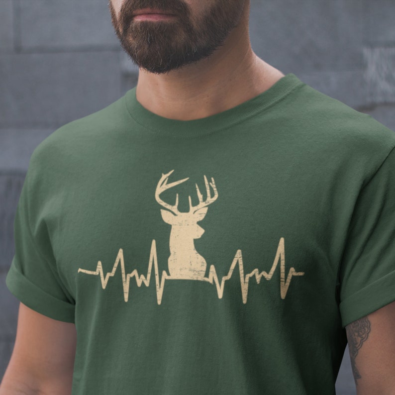 May include: A green t-shirt with a beige deer silhouette and a heartbeat graphic. The deer has antlers and is facing to the right.