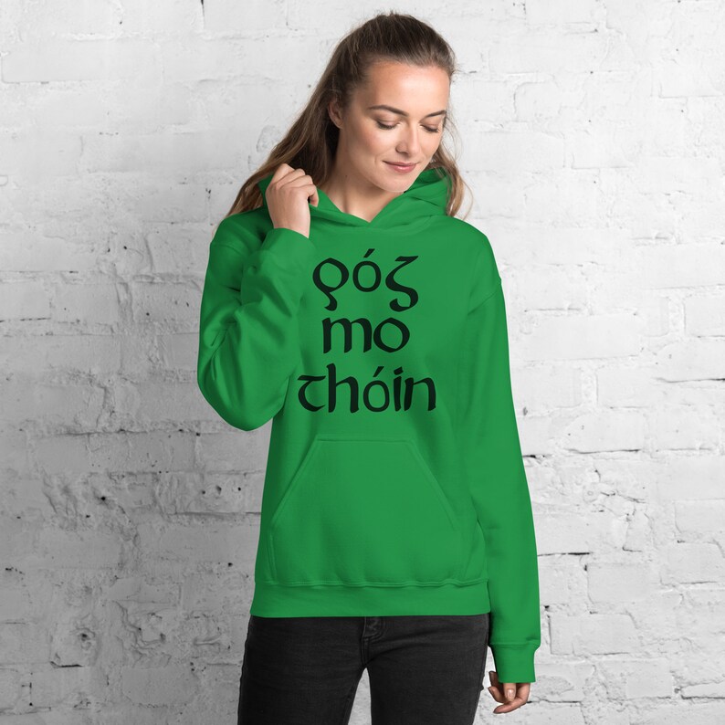 Puede incluir: Una sudadera con capucha verde brillante con un bolsillo delantero y una capucha con cord&oacute;n. La sudadera con capucha presenta texto negro en una fuente estilizada. La persona de la imagen lleva pantalones negros.