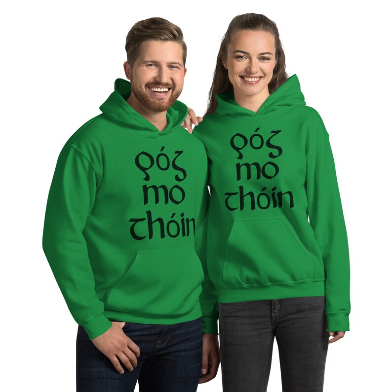 Puede incluir: Dos personas con sudaderas con capucha verdes a juego. Cada sudadera tiene el texto "G&oacute;s mo ch&oacute;in" en negro. Las sudaderas tienen un bolsillo delantero y una capucha. Las personas est&aacute;n sonriendo.