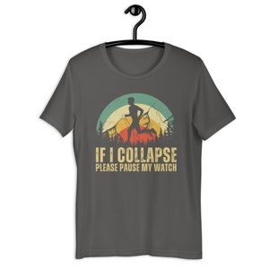 May include: A dark gray t-shirt with a vintage-style graphic of a runner in front of a mountain range. The text "IF I COLLAPSE PLEASE PAUSE MY WATCH" is printed below the graphic.