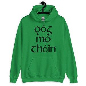 Puede incluir: Una sudadera con capucha verde con el texto negro "f&oacute;s mo ch&oacute;in". La sudadera tiene un bolsillo delantero y una capucha con cord&oacute;n. El logotipo de la marca Gildan es visible en la capucha.