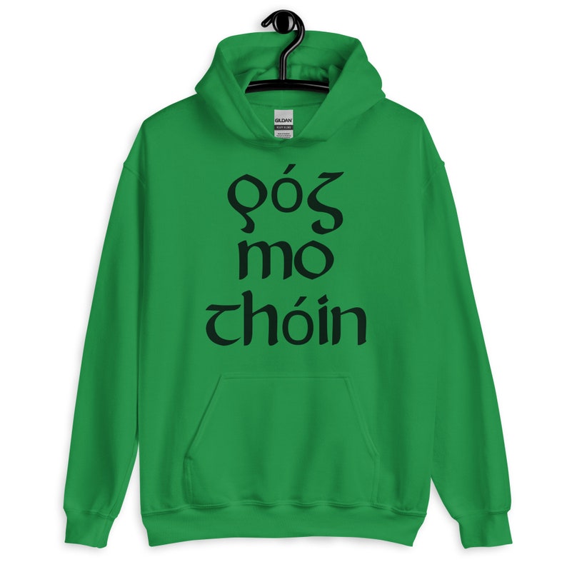 Puede incluir: Una sudadera con capucha verde con el texto negro "f&oacute;s mo ch&oacute;in". La sudadera tiene un bolsillo delantero y una capucha con cord&oacute;n. El logotipo de la marca Gildan es visible en la capucha.