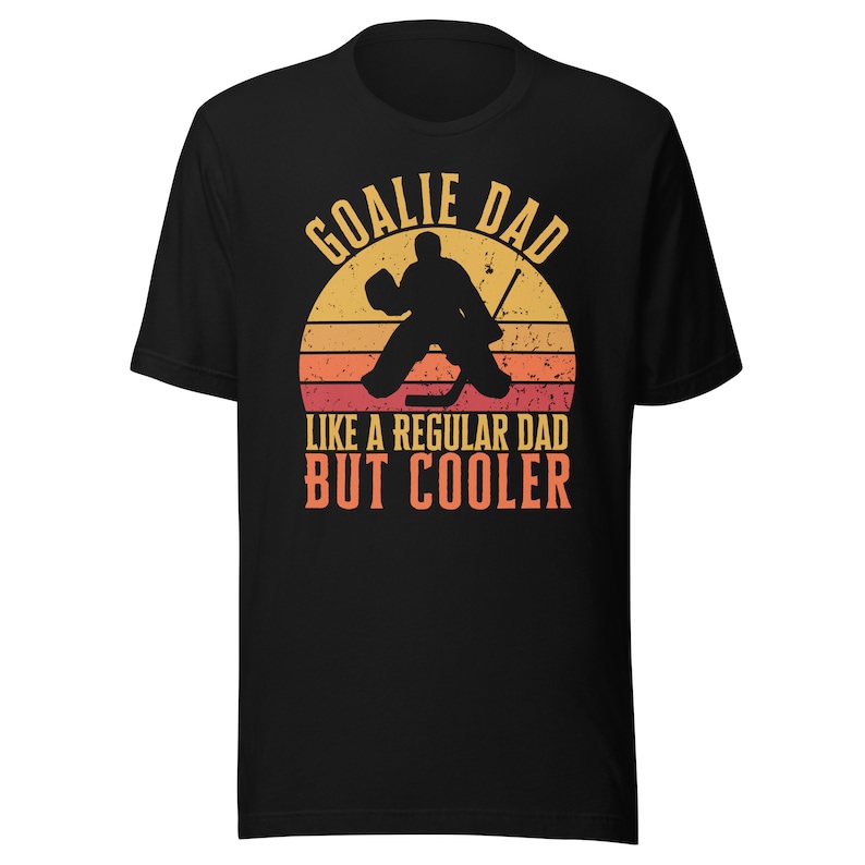 May include: Black t-shirt with a retro-style graphic of a hockey goalie in front of a sunset. The text reads "Goalie Dad Like a Regular Dad But Cooler."