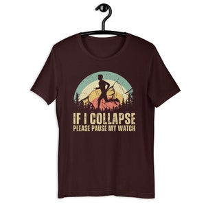 May include: A maroon t-shirt with a vintage-style graphic of a runner in front of mountains. The text "IF I COLLAPSE PLEASE PAUSE MY WATCH" is printed below the graphic.