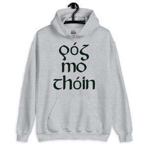 Puede incluir: Una sudadera con capucha gris claro con un bolsillo delantero y una capucha con cord&oacute;n. La sudadera con capucha presenta texto verde oscuro en una fuente estilizada. El texto dice "GOS MO CHOIN". La sudadera con capucha est&aacute; colgada de una percha negra.