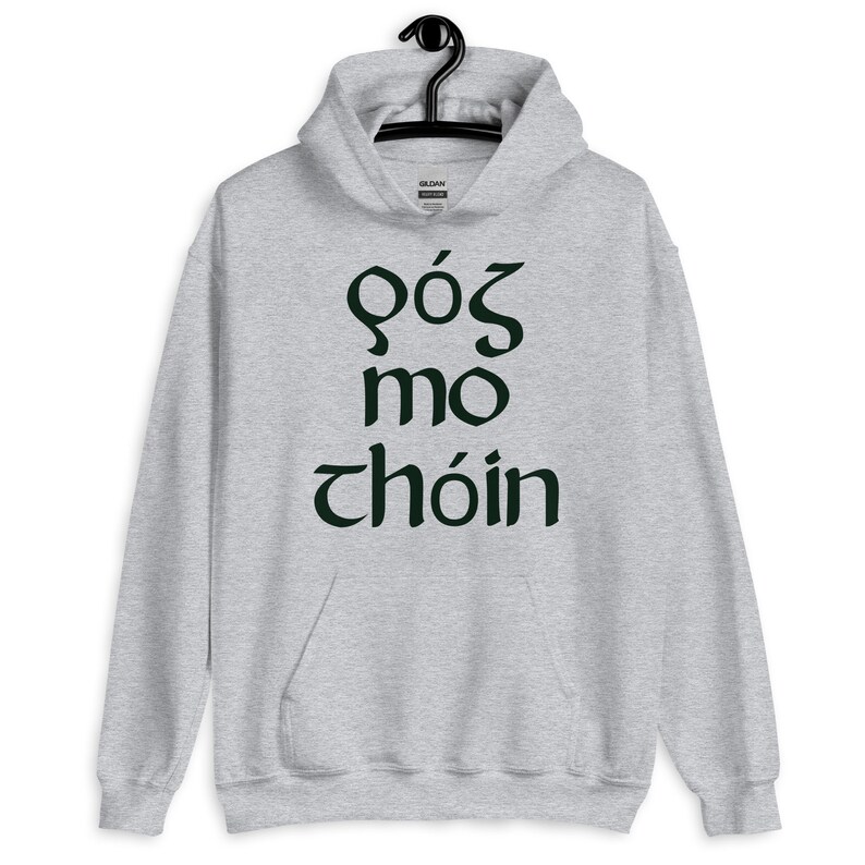 Puede incluir: Una sudadera con capucha gris claro con un bolsillo delantero y una capucha con cord&oacute;n. La sudadera con capucha presenta texto verde oscuro en una fuente estilizada. El texto dice "GOS MO CHOIN". La sudadera con capucha est&aacute; colgada de una percha negra.