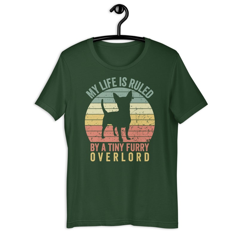 Op de afbeelding: Een groen T-shirt met een vintage-stijl afbeelding van een chihuahua voor een zonsondergang. De tekst luidt "Mijn leven wordt geregeerd door een kleine harige overlord."