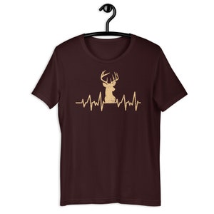 May include: A maroon t-shirt with a brown deer silhouette and a heartbeat graphic. The deer has antlers and is facing to the right.