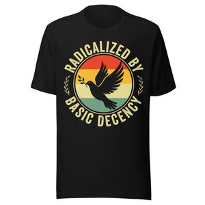 May include: Black t-shirt with a circular design featuring a dove carrying an olive branch, set against a retro sunset gradient. The text reads "RADICALIZED BY BASIC DECENCY" in a circular pattern.