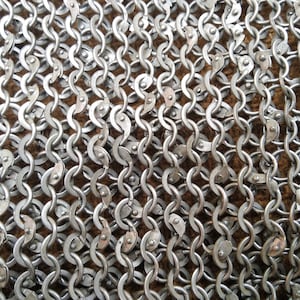 Può includere: Primo piano di una cotta di maglia argentata, un tipo di armatura realizzata con anelli di metallo intrecciati.