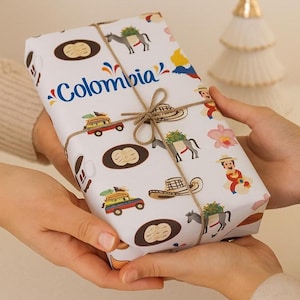 May include: A rectangular gift wrapped in white paper with a colorful pattern of Colombian cultural symbols, including donkeys, hats, and cars. The word "Colombia" is written in blue script. The gift is tied with twine.