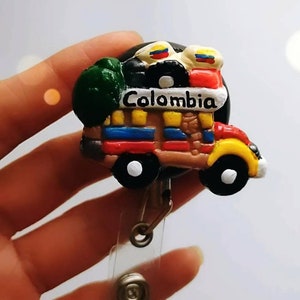 May include: A colorful, cartoon-style truck with the word "Colombia" on the side. The truck is carrying a green plant, a black and white record, and two Colombian flags. The truck is attached to a retractable badge holder.