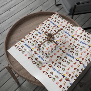 May include: A wrapped gift box and wrapping paper featuring a repeating pattern of Colombian cultural icons, including coffee cups, hats, and flowers. The gift is tied with a brown ribbon. A pair of scissors is also on the paper.