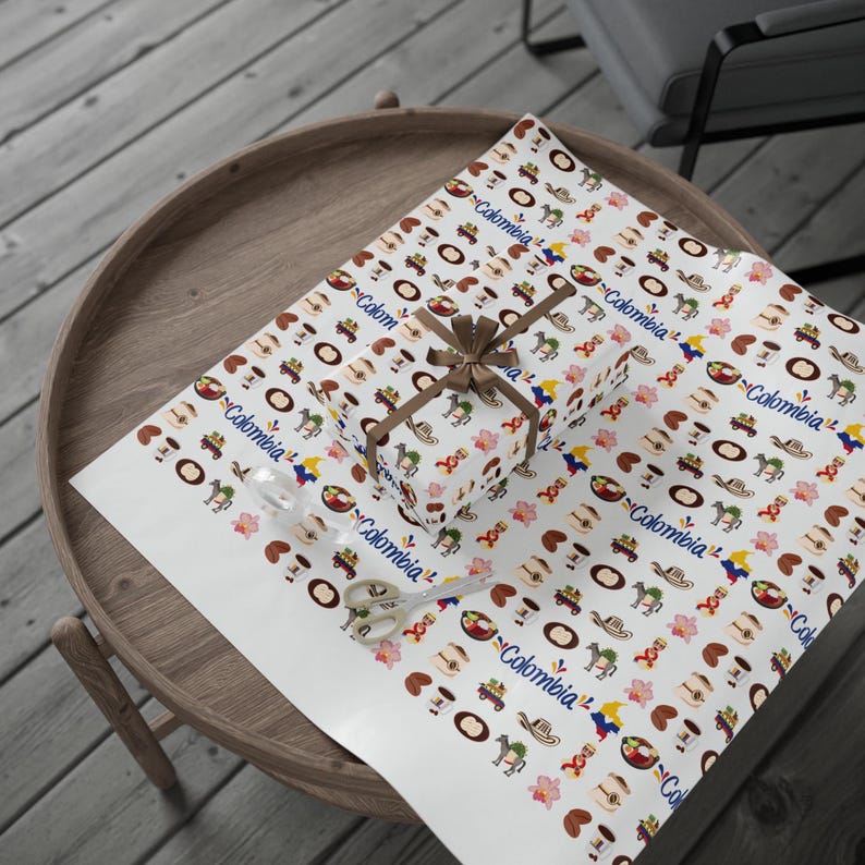 May include: A wrapped gift box and wrapping paper featuring a repeating pattern of Colombian cultural icons, including coffee cups, hats, and flowers. The gift is tied with a brown ribbon. A pair of scissors is also on the paper.