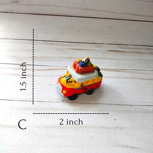 May include: A small, colorful, hand-painted ceramic bus figurine with luggage on the roof. The bus is approximately 2 inches long and 1.5 inches tall.