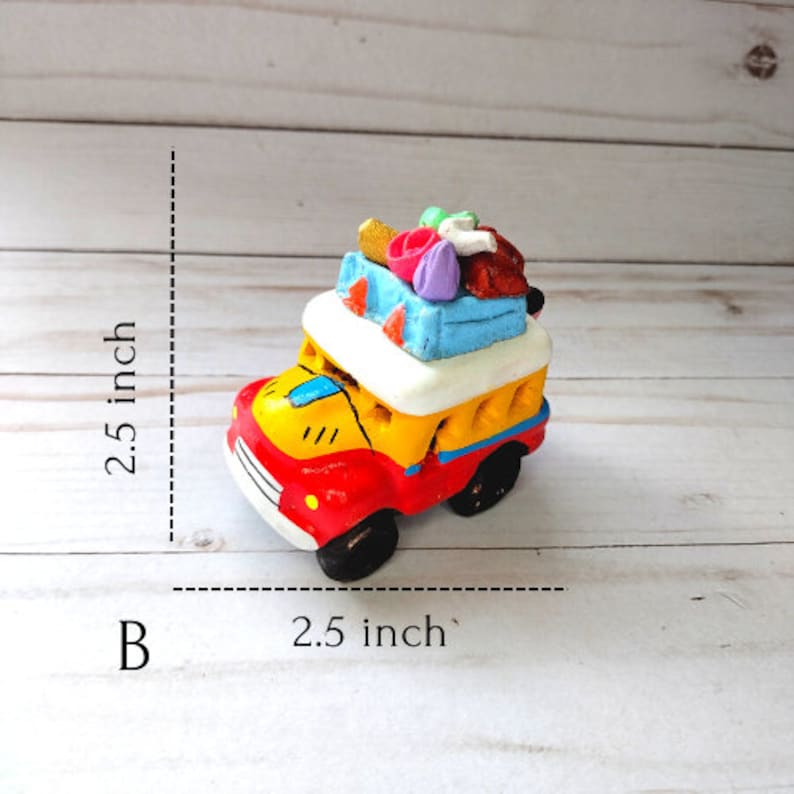 May include: A small, colorful, ceramic toy car with a red body, yellow sides, and a white roof. The car is loaded with luggage on top, including a blue suitcase, a pink suitcase, and a brown bag. The car is 2.5 inches wide and 2.5 inches tall.